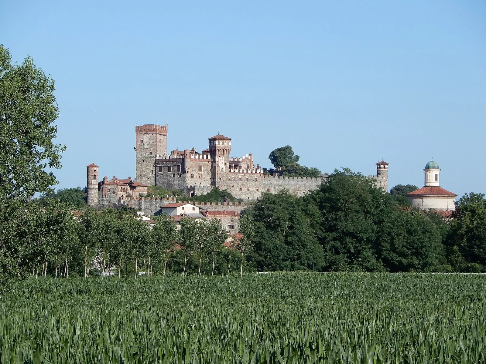 Il castello di Pavone Canavese con torri e mura merlate sulla collina, sopra un campo di grano verde