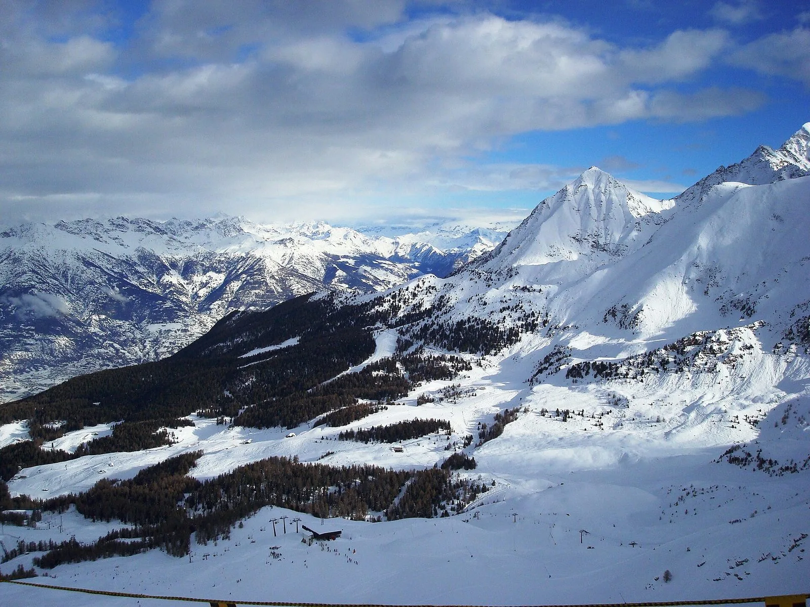 Panorama invernale delle piste di Pila in Valle d'Aosta, con boschi di conifere, impianti di risalita e montagne innevate